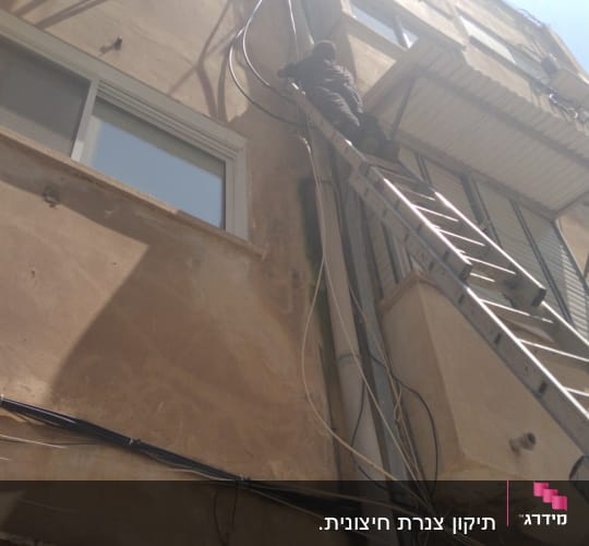 אדם על סולם מתקן צינורות על קיר בניין